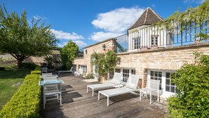 A wooden deck with white lounge chairs, a stone building with a turret, and a clear blue sky. - Villa Louise (Aloxe-Corton)