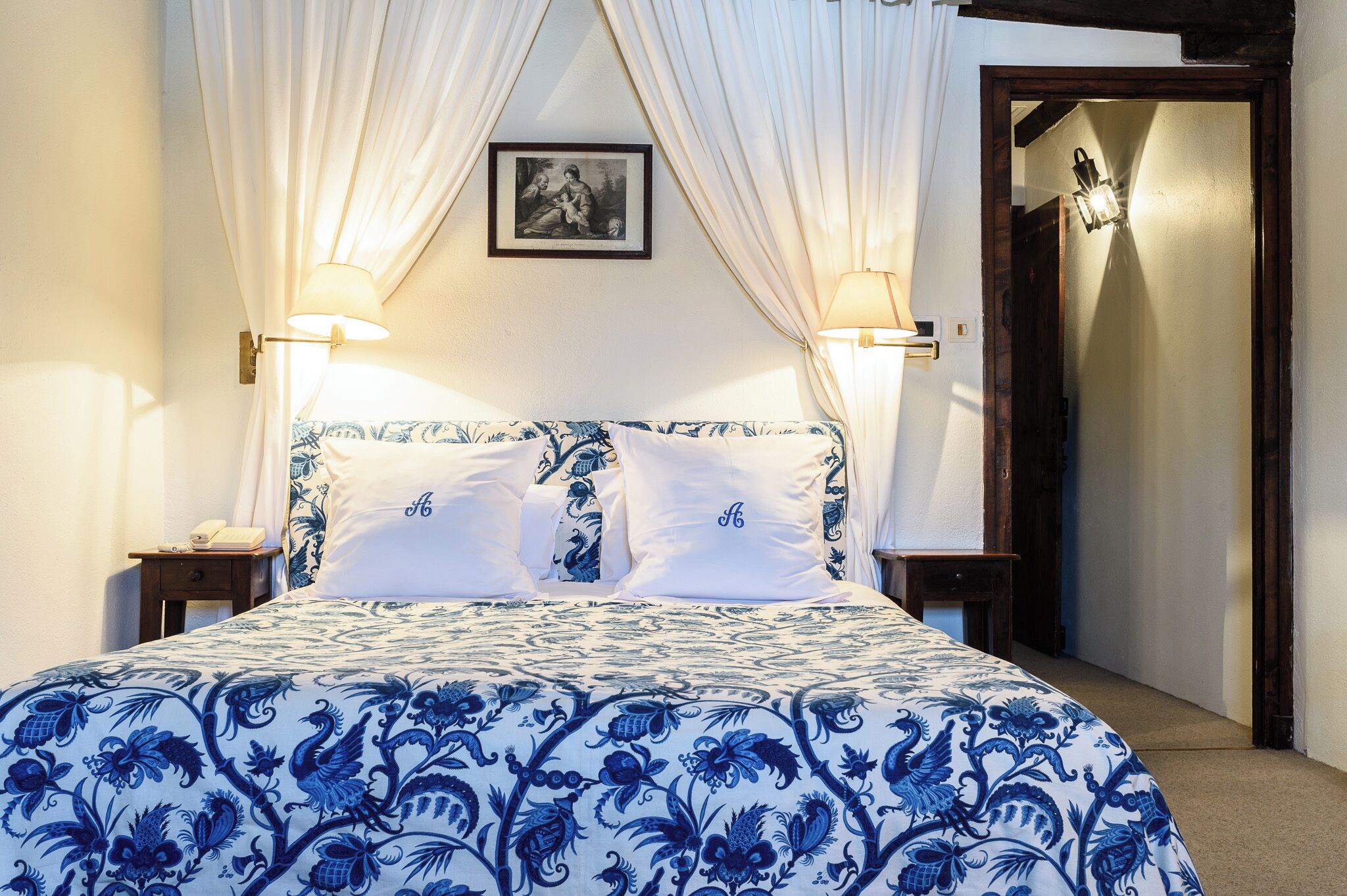 Una cama con una colcha azul estampada de flores, dos lámparas de noche y un cuadro en la pared.