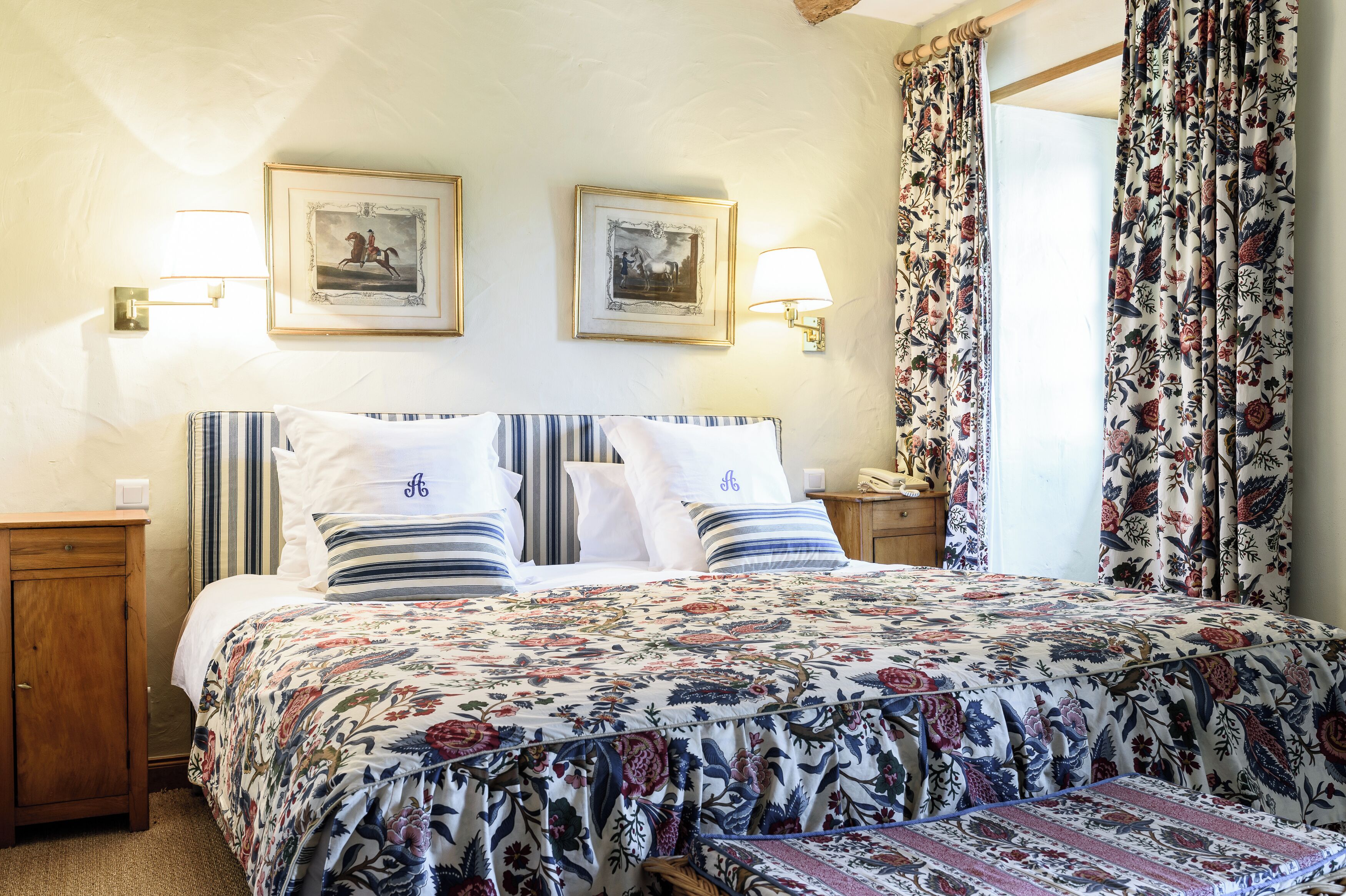 A neatly made bed with floral bedding, two wall-mounted lamps, and framed pictures above it.