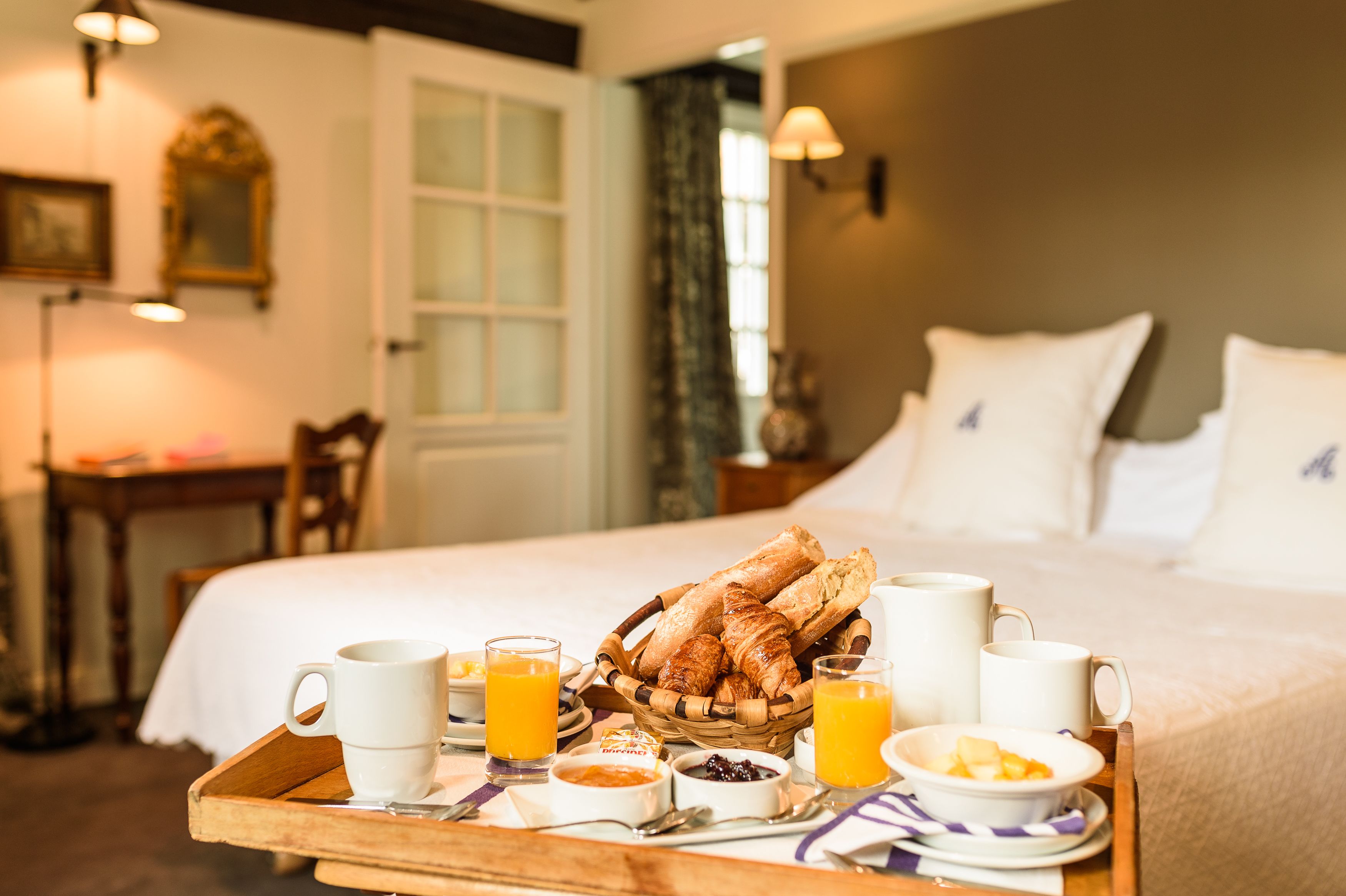 A breakfast tray with croissants, coffee cups, and orange juice on a wooden table in a hotel room.