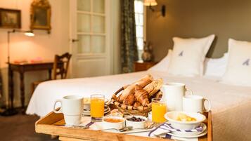 A breakfast tray with croissants, coffee cups, and orange juice on a wooden table in a hotel room.