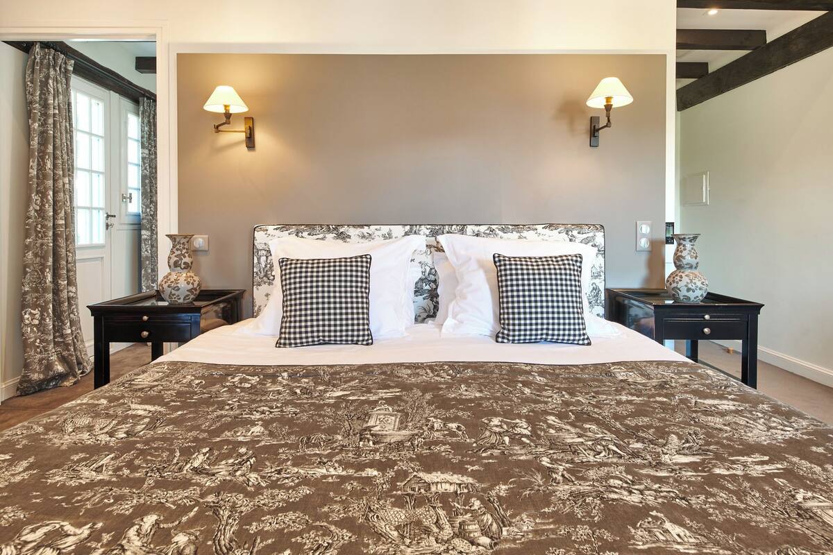 A bed with a patterned bedspread, two matching pillows, and two wall-mounted lamps.