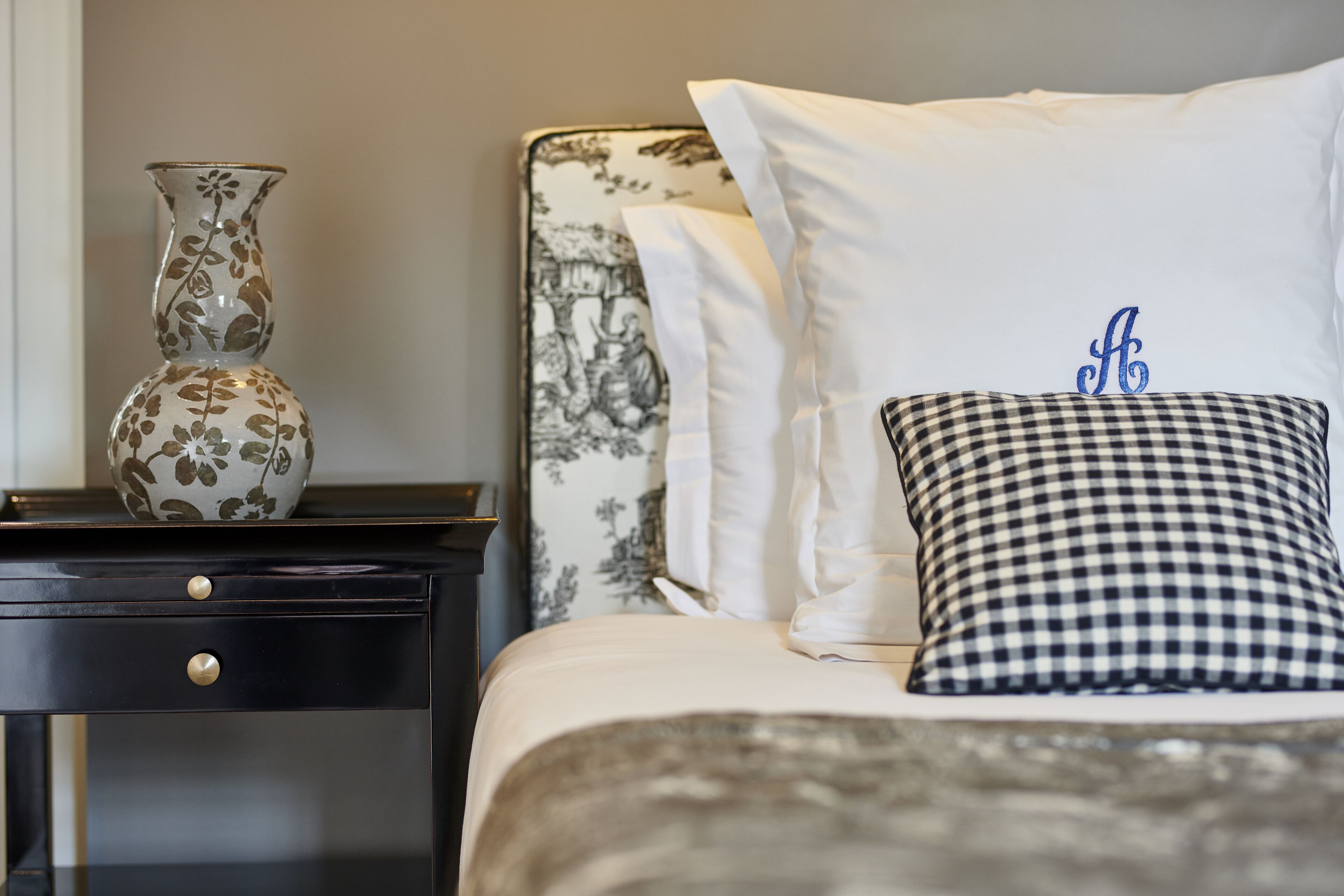 A neatly made bed with a checkered pillow and a vase on a bedside table.