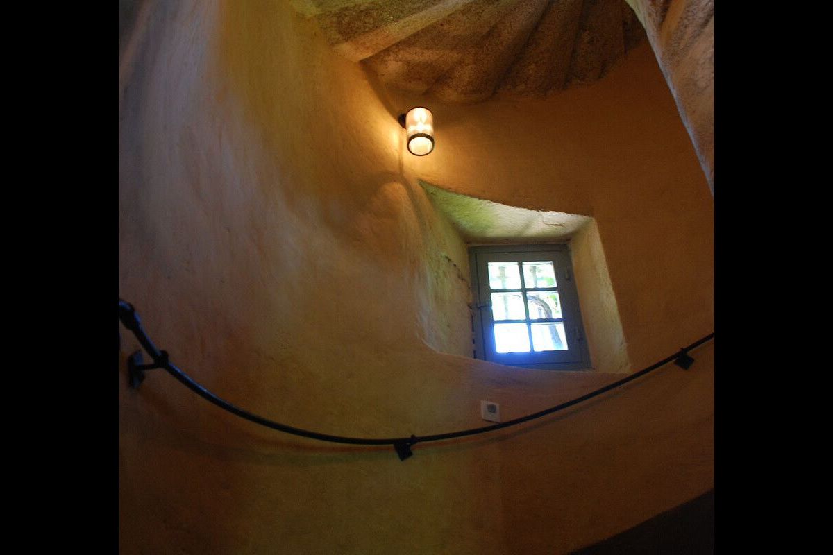 A room with a sloped ceiling, a small window with a view, and a wall-mounted light fixture.