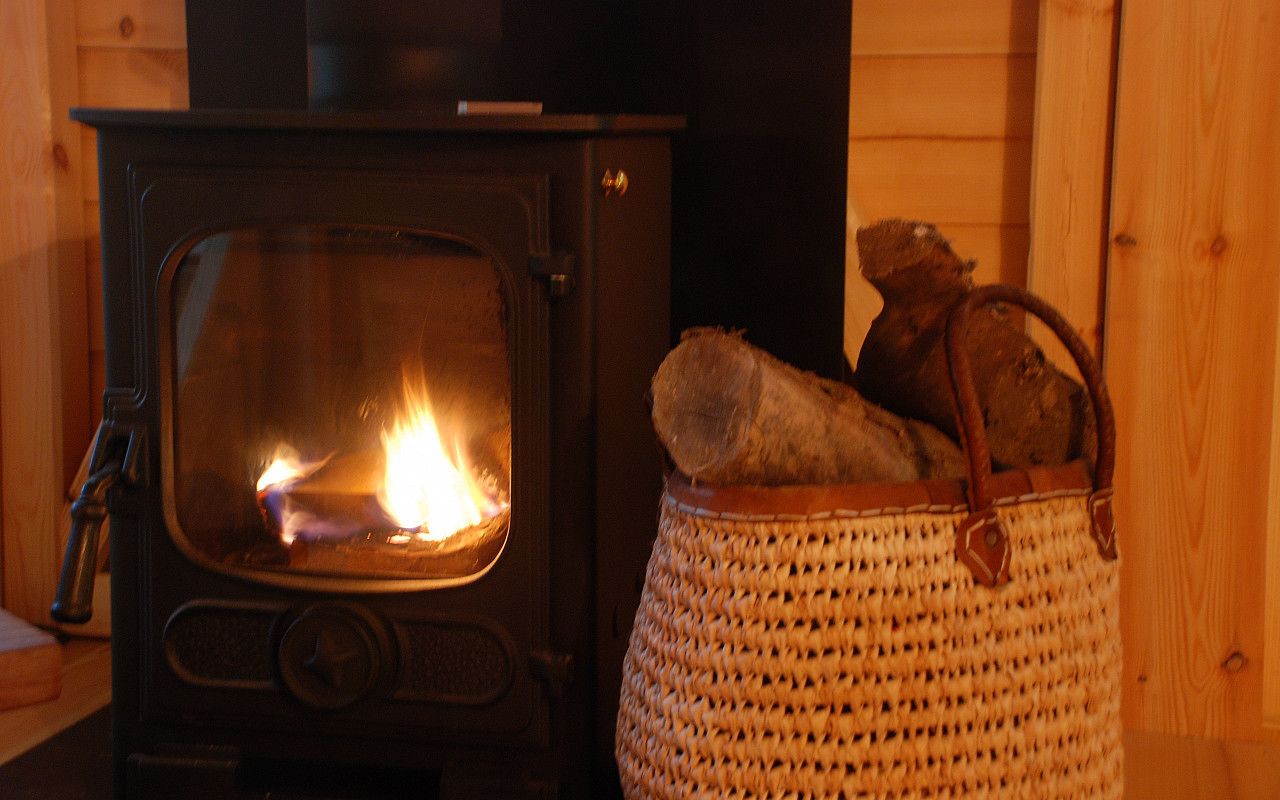 En vedeldad kamin med ved inuti och en flätad korg bredvid.