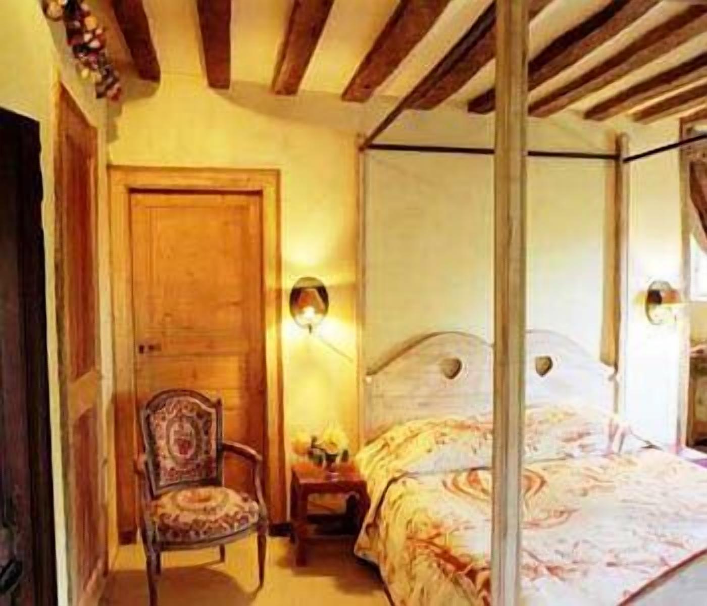 A bedroom with a four-poster bed, a wooden chair, and a nightstand with a lamp.