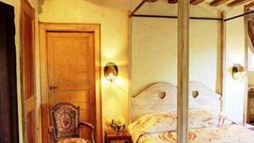 A bedroom with a four-poster bed, a wooden chair, and a nightstand with a lamp.