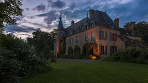 Ein großes, historisches Gebäude mit einem markanten Turm, umgeben von gepflegten Gärten und einem Rasen.