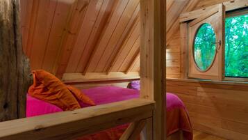 Une cabane en bois avec un lit en mezzanine, une fenêtre donnant sur la verdure et une rambarde en bois.