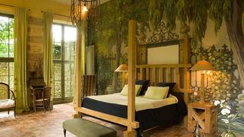 Una cama con dosel, un banco, un escritorio y una silla en una habitación con un mural de árboles y flores.