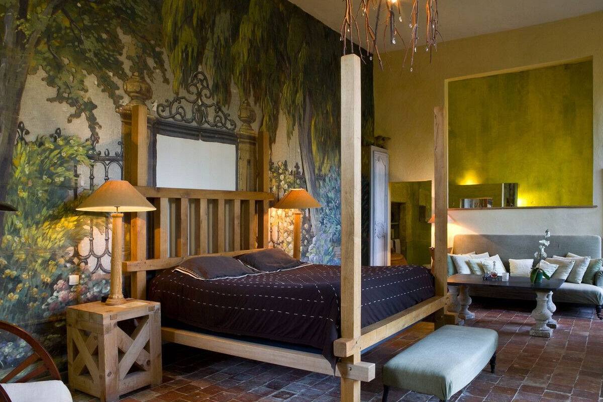 Een slaapkamer met een groot bed, twee nachtkastjes, een bankje, een sofa en een muur met een muurschildering.