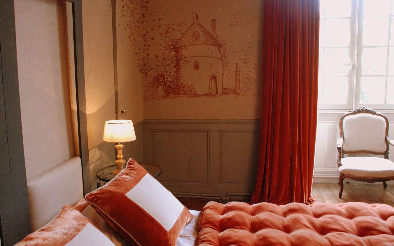 Een slaapkamer met een bed, een stoel, een lamp en een muur met een tekening van een huis.