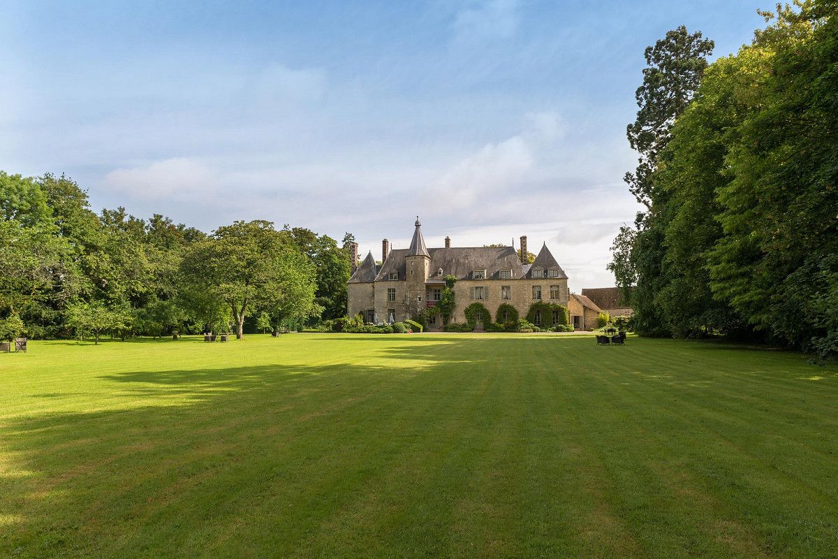 A large, historic building with a symmetrical facade, surrounded by a well-maintained lawn and mature trees.