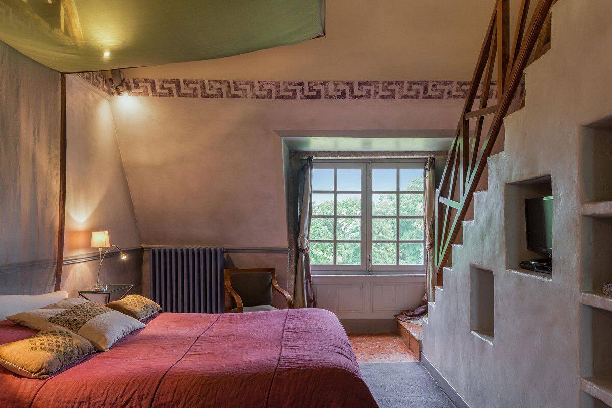 Een slaapkamer met een bed, een raam, een radiator, een televisie en een trap.