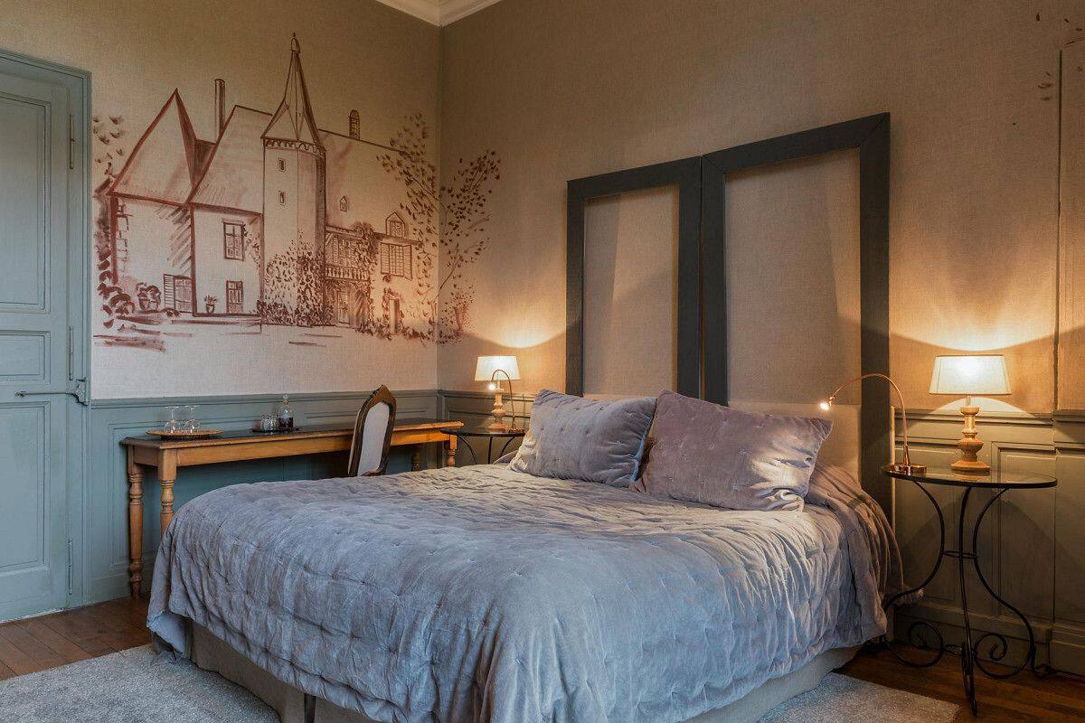 Een slaapkamer met een groot bed, twee nachtkastjes met lampen, een bureau met stoel, en een wanddecoratie.