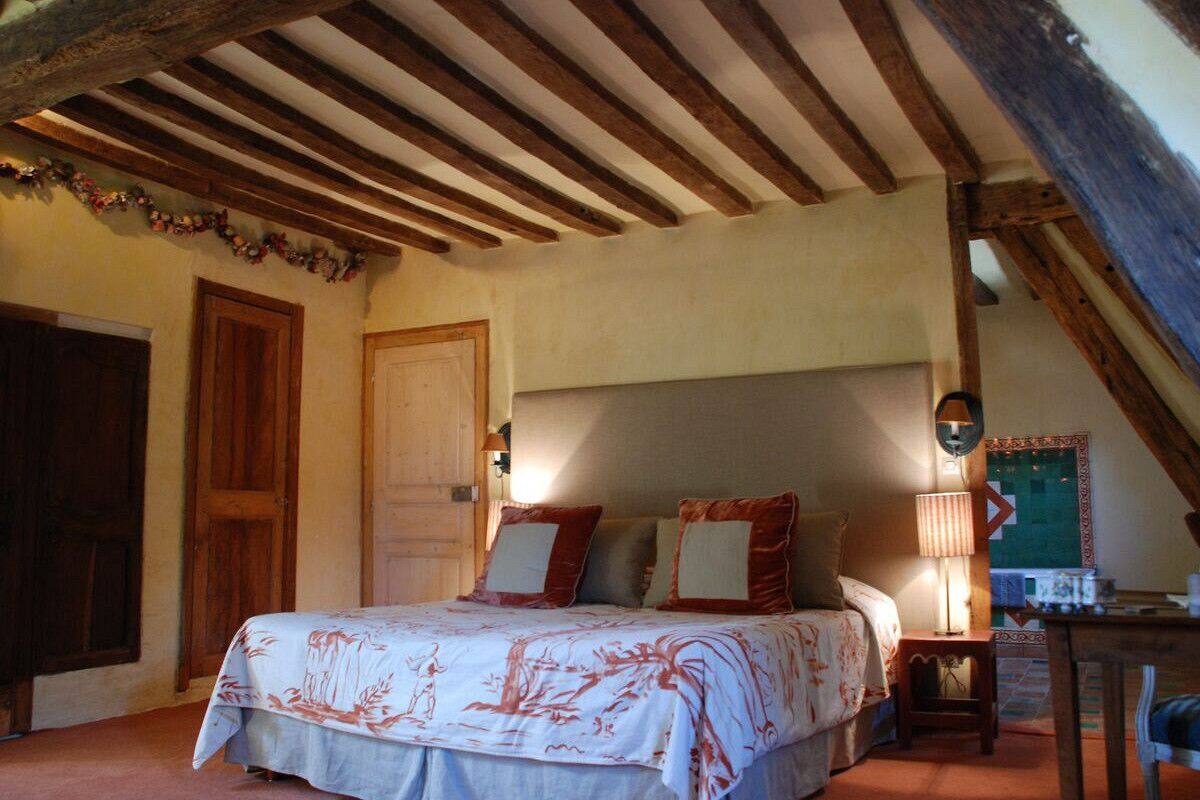 Een slaapkamer met een houten plafond, een bed met een bloemenbedekking, een nachtkastje en een stoel.