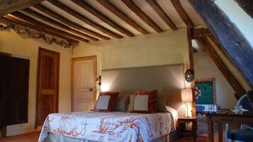Une chambre avec un plafond en bois, un lit recouvert d’une couvre-lit à motifs floraux, une table de chevet et une chaise.