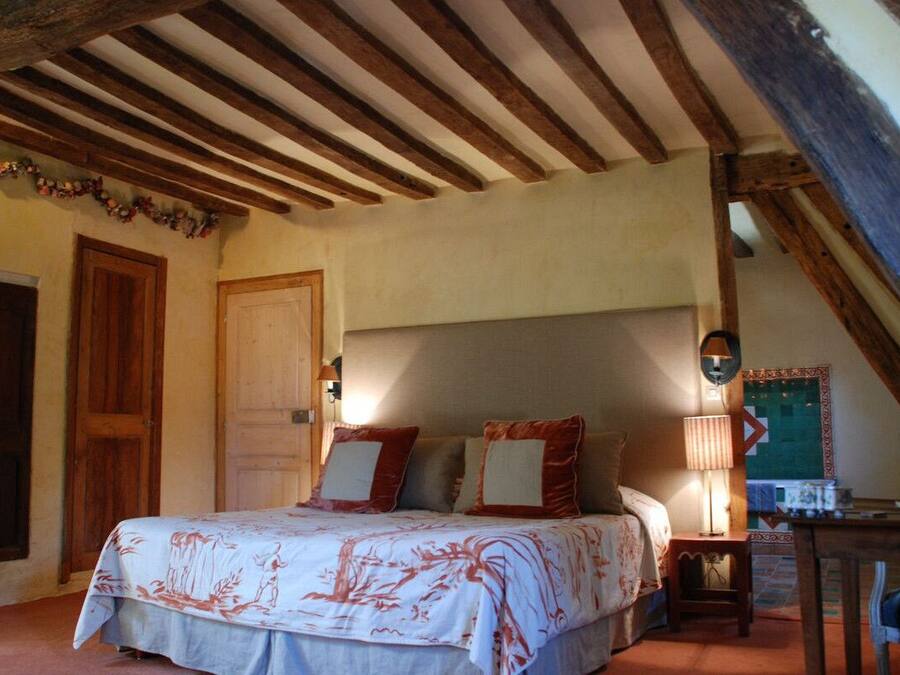 Une chambre avec un plafond en bois, un lit recouvert d’une couvre-lit à motifs floraux, une table de chevet et une chaise.