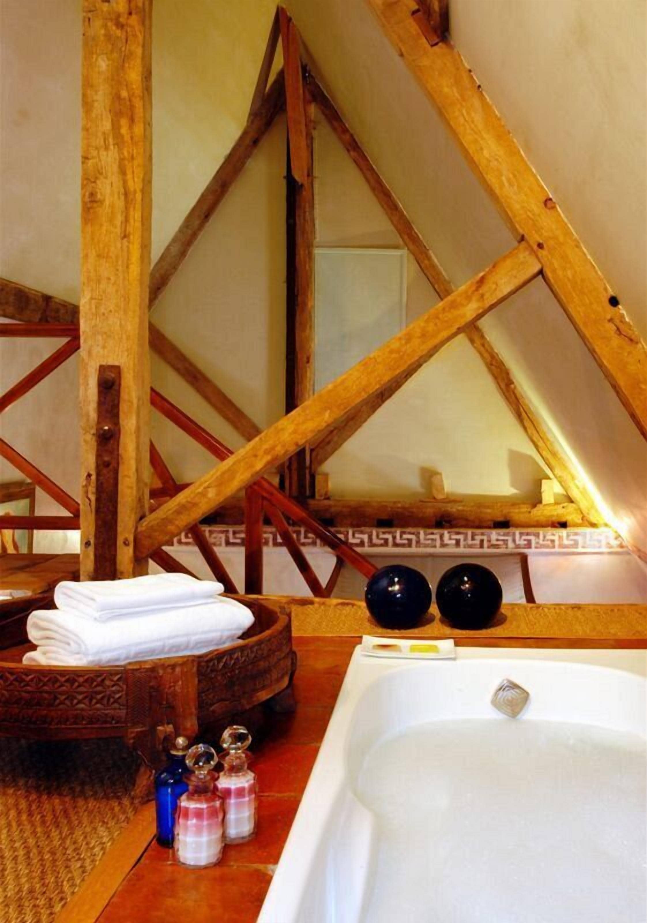 Une salle de bain rustique avec une baignoire en bois, un banc en bois et une petite table ronde sur laquelle sont posées des serviettes et des articles de toilette.