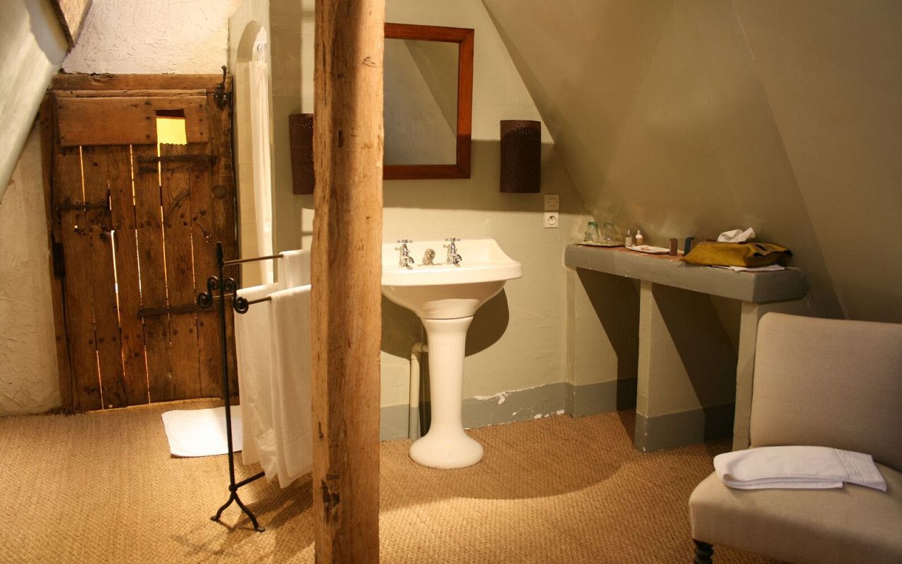 Un baño pequeño y acogedor con una puerta de madera, un lavamanos blanco sobre pedestal y una toalla en una silla.
