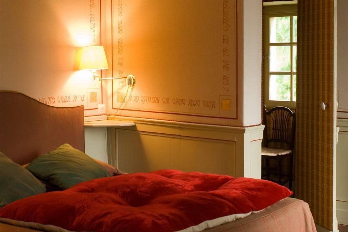 Een slaapkamer met een bed, een nachtkastje met een lamp, een stoel en een raam.
