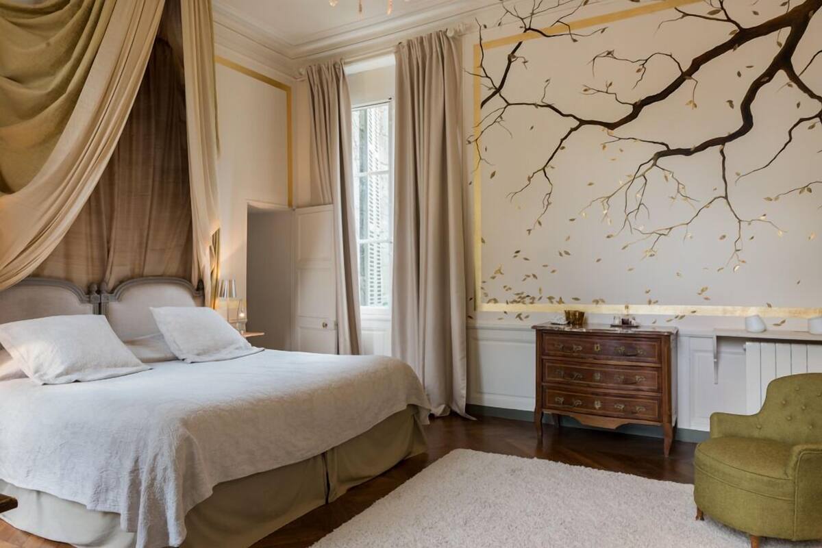 Een slaapkamer met een groot bed, een kaptafel, een groene fauteuil en een muur met een ontwerp van een tak.