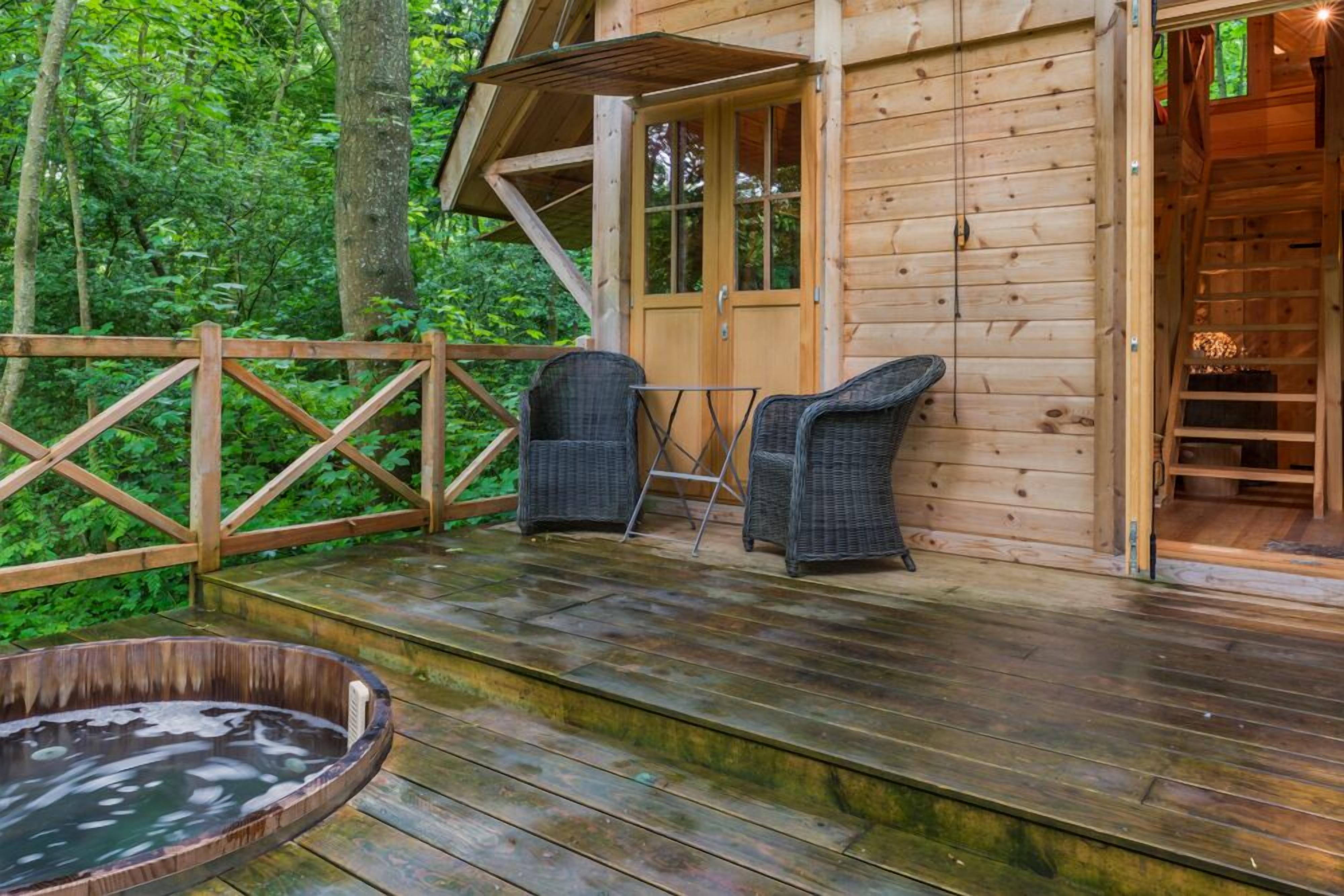 Una cabaña de madera con terraza, dos sillas de mimbre y un jacuzzi.