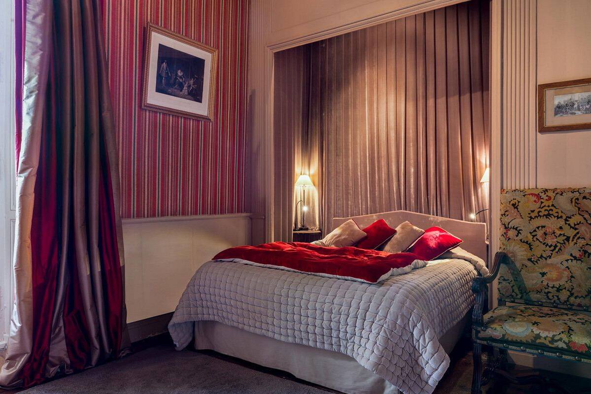 Een slaapkamer met een bed, een stoel en gordijnen.