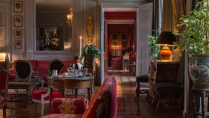 Ein luxuriöses Zimmer mit einer roten Couch, verzierten Stühlen, einem Holztisch und einer großen Pflanze.