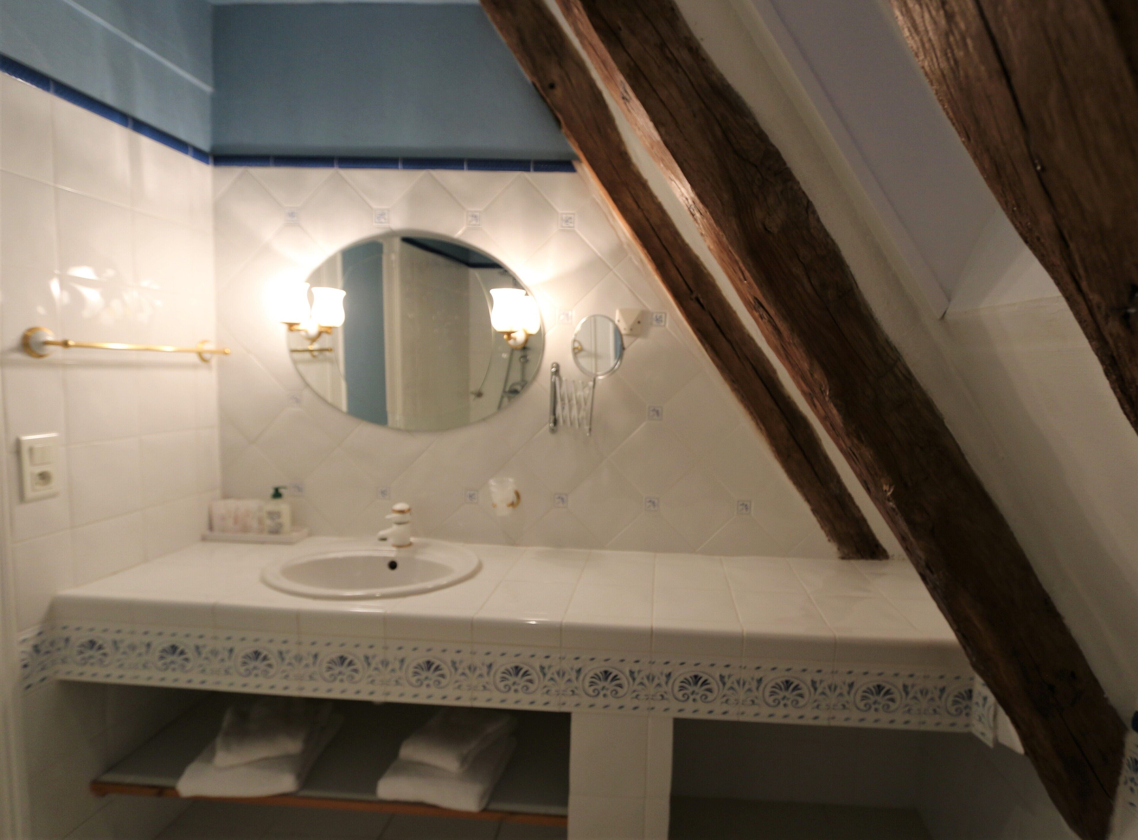 Un baño con lavamanos blanco, espejo y toallero.