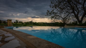 Una piscina con borde de piedra, rodeada de follaje y árboles.