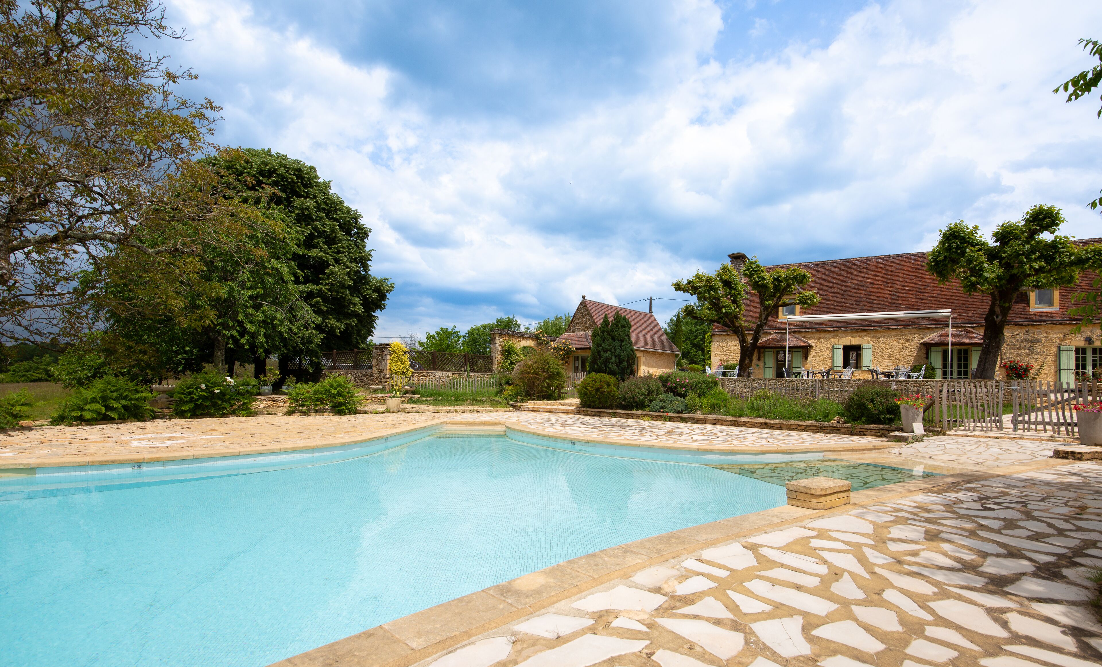 A swimming pool with stone tiles, surrounded by a stone wall and a wooden fence.