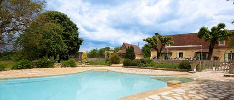 A swimming pool with stone tiles, surrounded by a stone wall and a wooden fence.