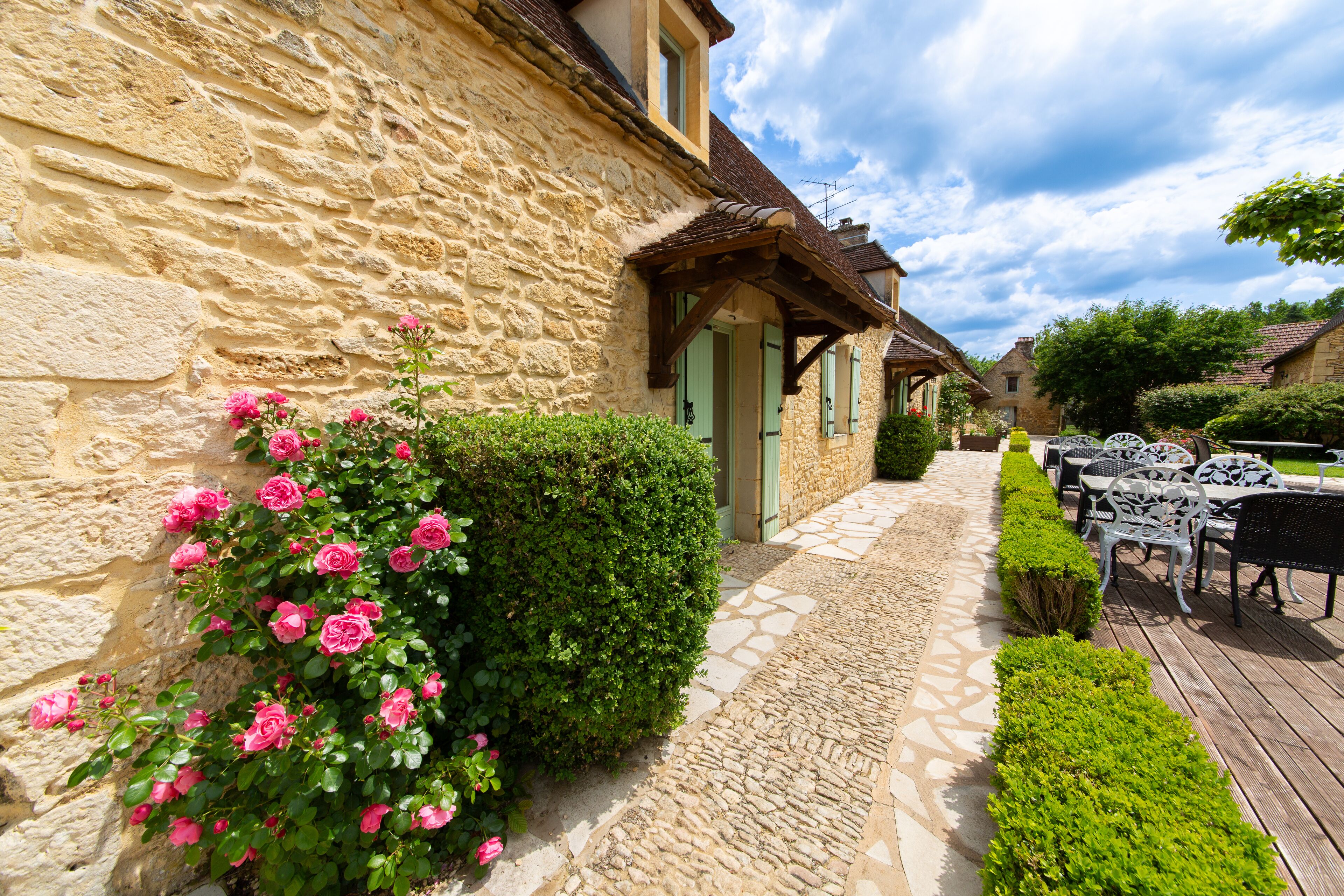 A stone building with a paved walkway, outdoor seating, and a well-maintained garden with pink flowers.