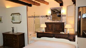 A bedroom with a wooden headboard, a large mirror, a bedside table with lamps, and a dresser.
