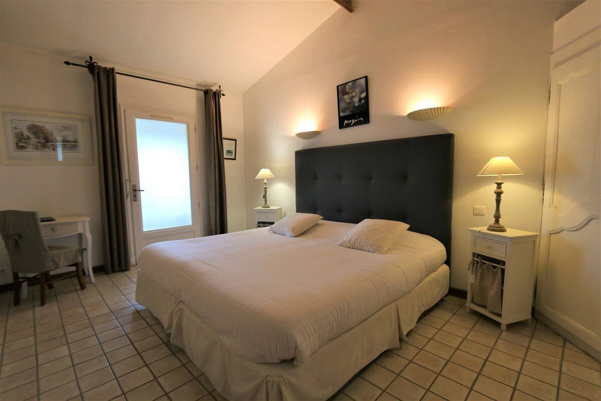 A neatly arranged bedroom with a large bed, two bedside lamps, a desk, and a chair.