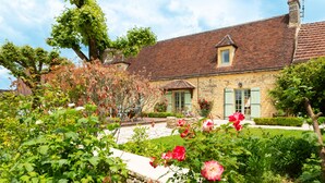 A stone house with a tiled roof, a garden with roses, and a clear sky. - Hôtel de la Ferme Lamy (Meyrals)