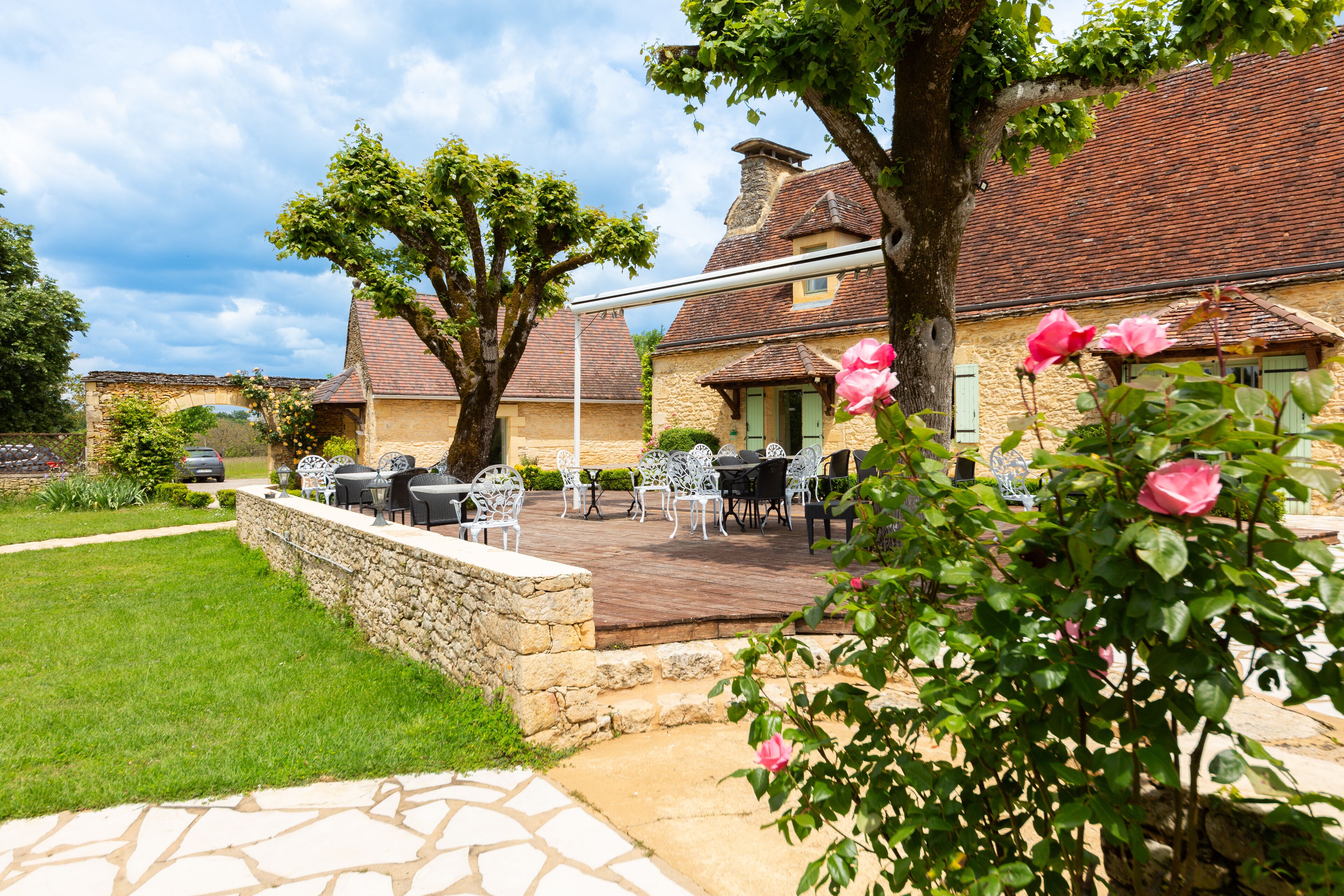 A stone patio with outdoor seating, a stone wall, and a building with a tiled roof.