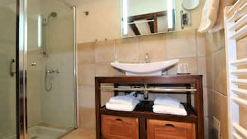 A bathroom with a glass shower enclosure, a white sink, and a wooden vanity with towels.