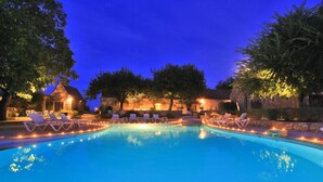A swimming pool with lounge chairs and string lights, surrounded by trees and stone buildings. - Hôtel de la Ferme Lamy (Meyrals)