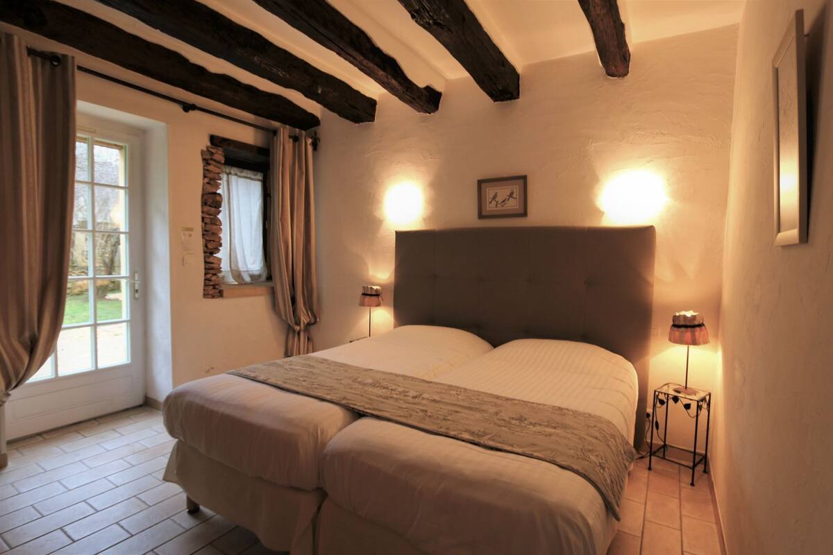 A bedroom with a large bed, two bedside lamps, a framed picture on the wall, and a window with curtains.