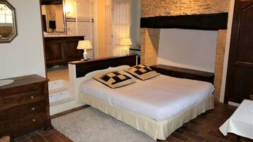 Un dormitorio con una cama, mesitas de noche, un tocador, un espejo y una pared de piedra.