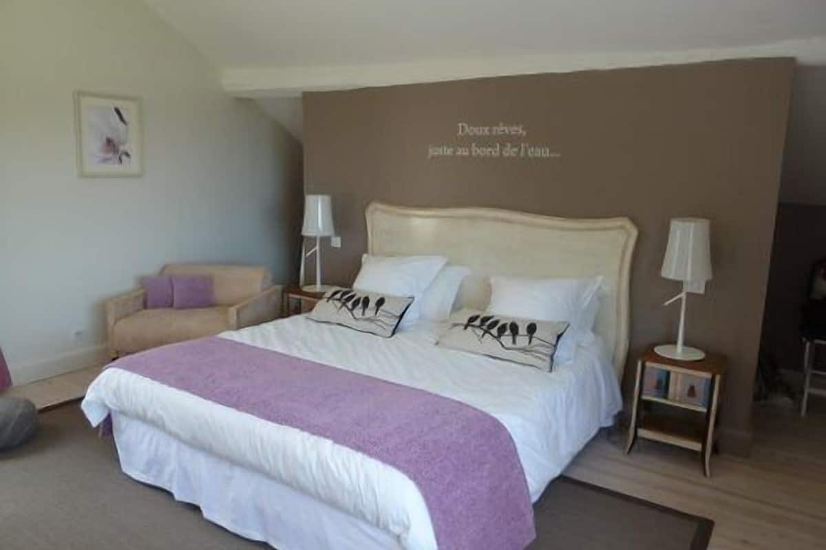 A bedroom with a large bed, two bedside tables, a chair, and a wall with a decorative text.