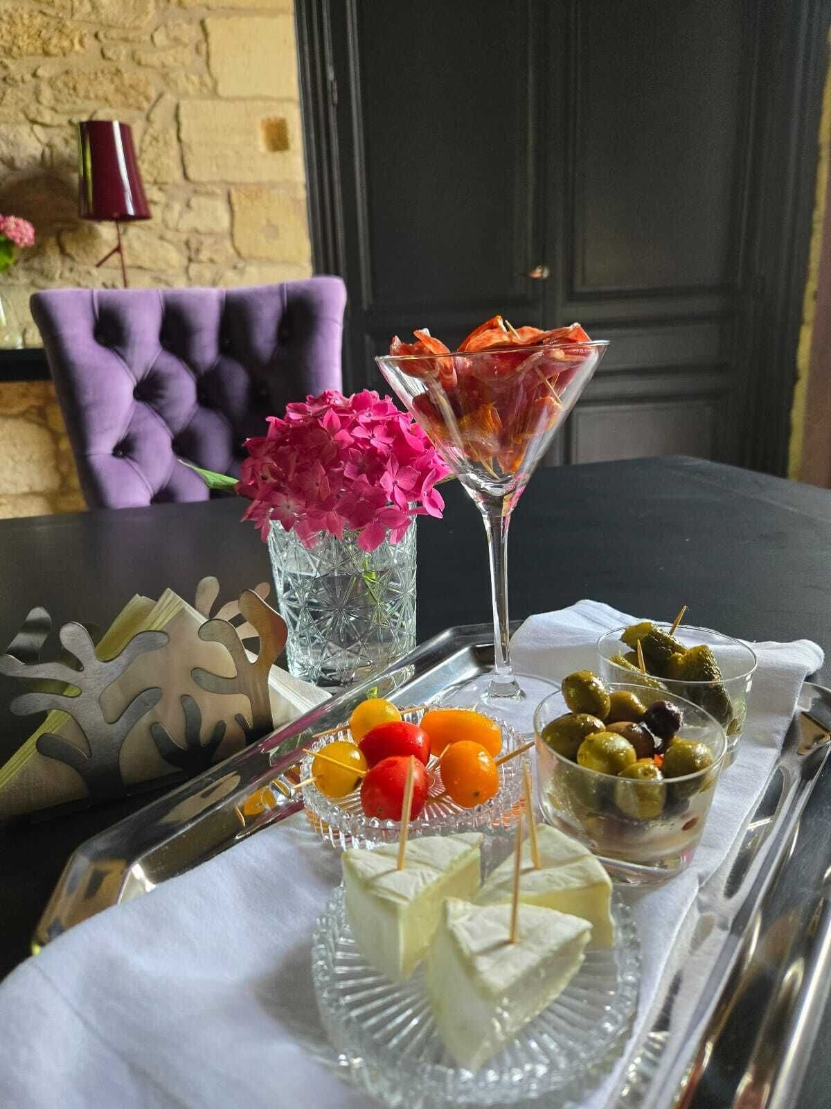 A table set with a variety of appetizers including cheese cubes, olives, and skewered fruits, accompanied by a martini glass and a vase with pink flowers.