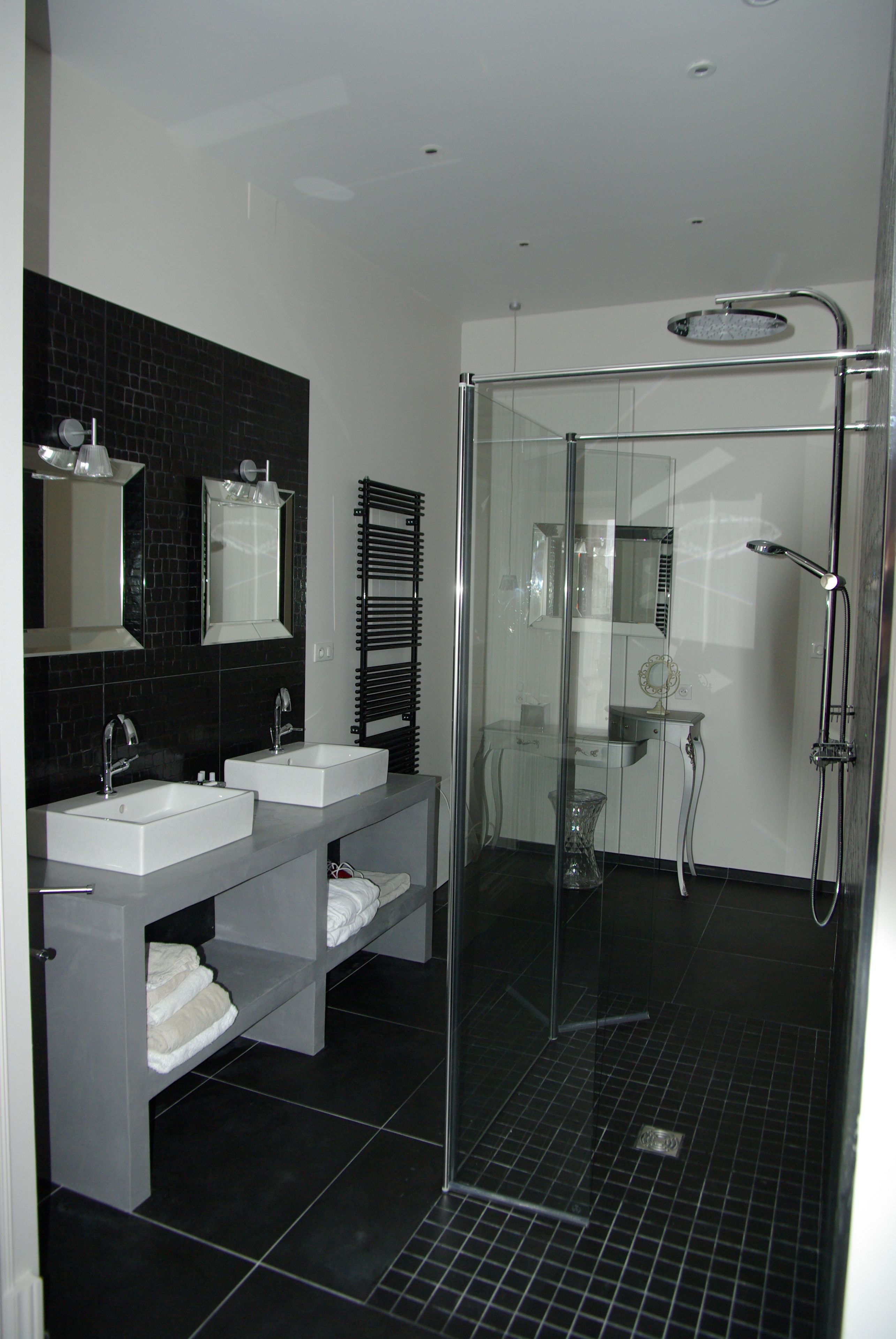Un baño moderno con dos lavamanos, cabina de ducha de cristal y suelo de baldosas negras.