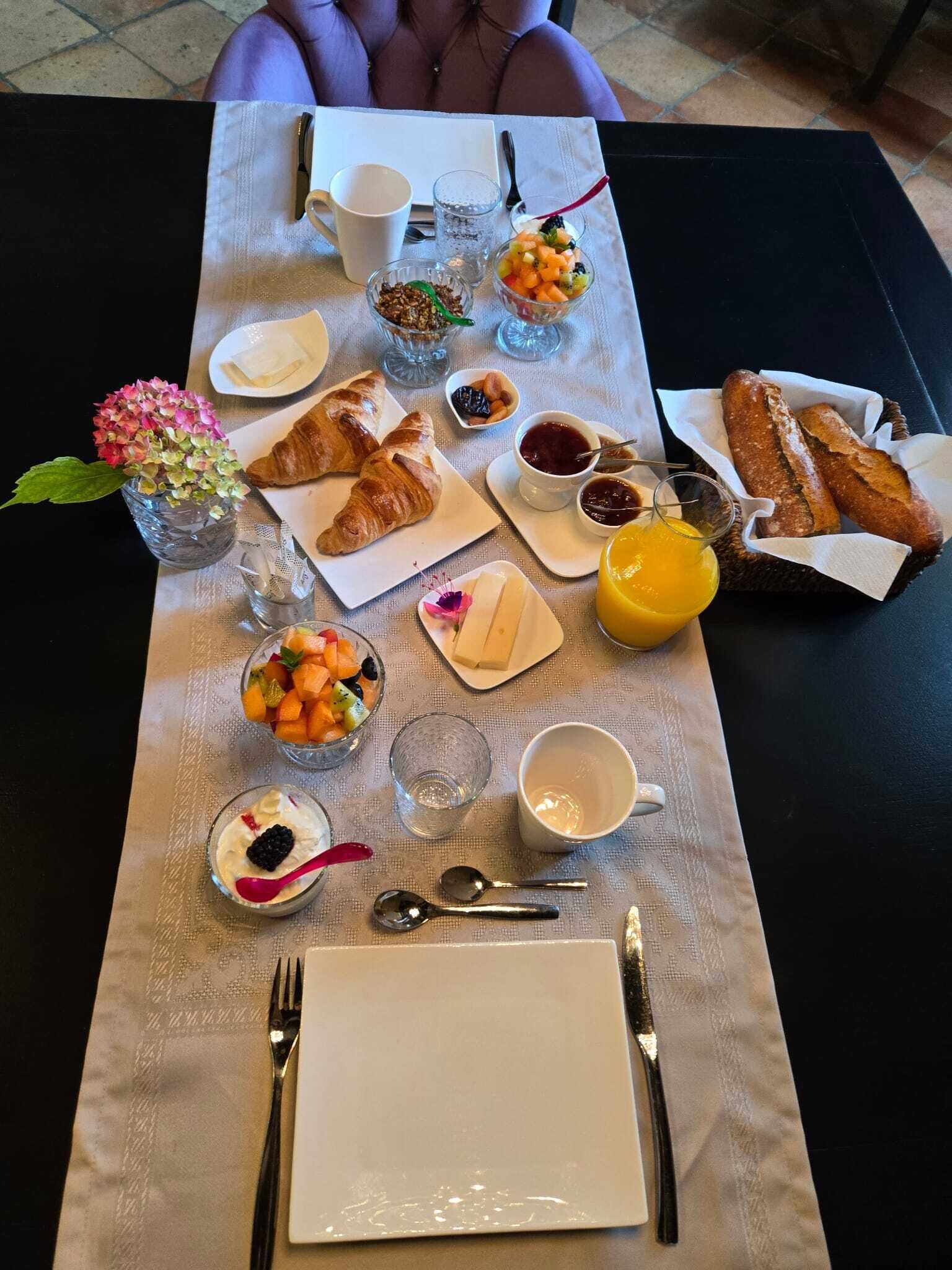 Une table de petit-déjeuner avec des croissants, des fruits, de la confiture et du jus.
