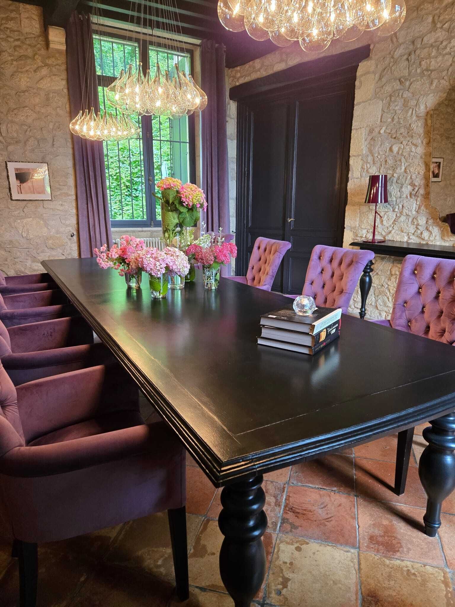 Un espace repas avec une longue table, des chaises à revêtement violet et un lustre.