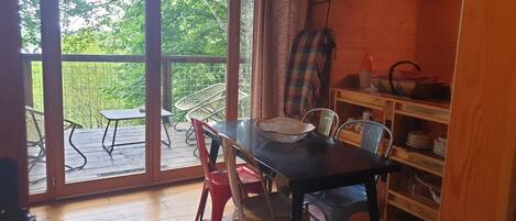 A dining area with a table and chairs, a woven basket, and a wooden shelf with dishes.