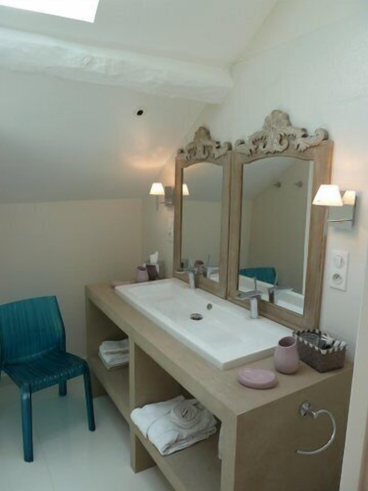 Een badkamer met een grote spiegel, een wastafel, een stoel en een handdoekhouder.
