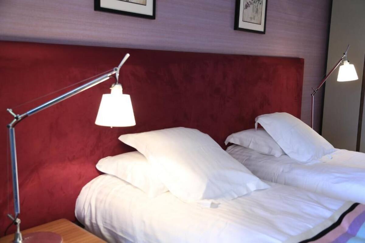 A neatly made bed with white linens and pillows, a red headboard, and two bedside lamps.